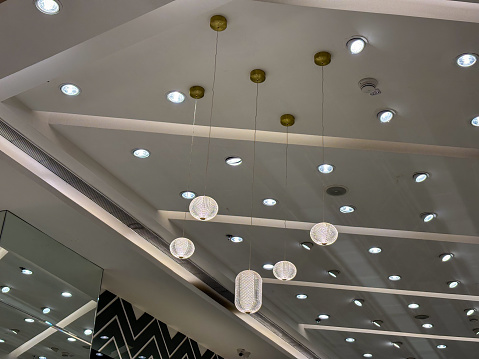 This image shows a spacious room filled with numerous modern lights hanging from the ceiling, illuminating the area with a bright and even glow. The lights vary in size and shape, creating an interesting visual display.