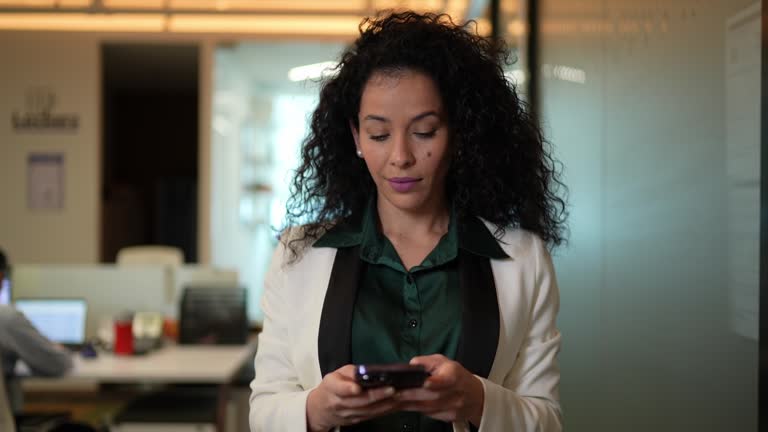 Mid adult businesswoman using mobile phone and walking through the office