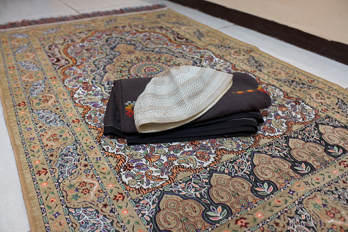 A sarong with a folded skullcap on top of a prayer mat. Pray equipment Ramadan month