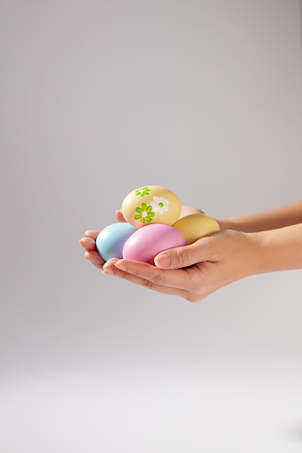 Beautiful female hand model is carrying several Easter eggs in many colours and patterns against white background. Easter is one of the principal holidays, or feasts, of Christianity