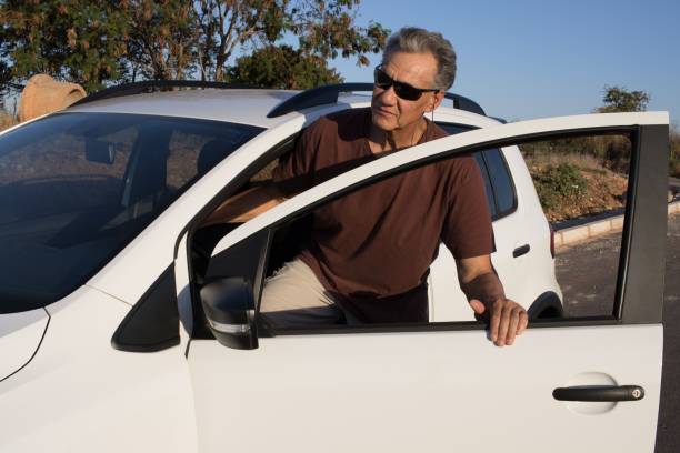 A man stands beside a white car, gazing out of the window