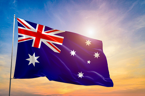 The national flag of Australia flutters in the wind against a clear blue sky with sunshine