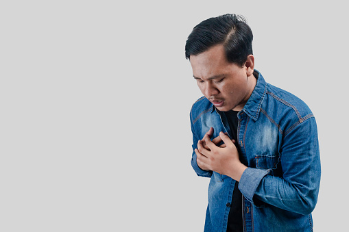 Young Asian man having chest pain or heart trouble and pressing his chest on isolated white background.