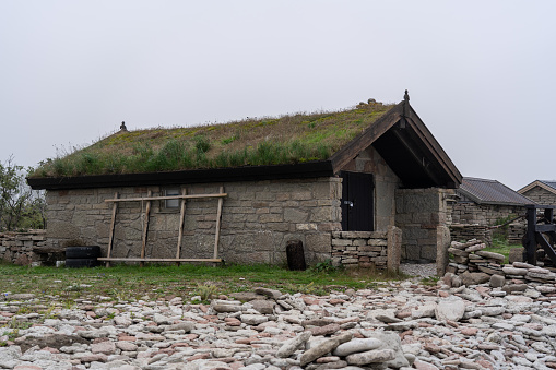 A small stone building with a lush green roof, surrounded by rocks in the foreground