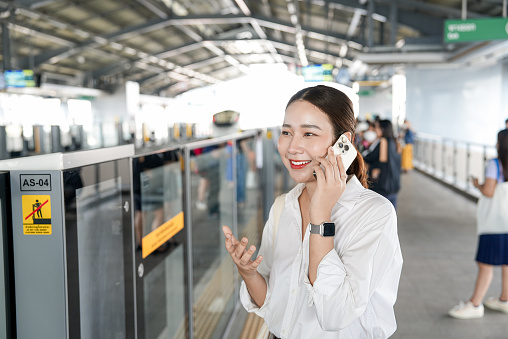 Young woman standing and talking on the phone while waiting for the BTS train
