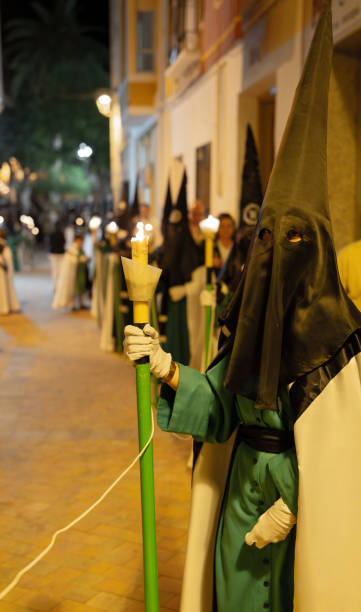 porträt eines unbekannten "capirucho"-anhängers, der den weg in einer prozession der stechpalmenwoche erhellt. vertikale aufnahme, grünes schwarz-weißes gewand und kapuze - church religion spirituality holly stock-fotos und bilder