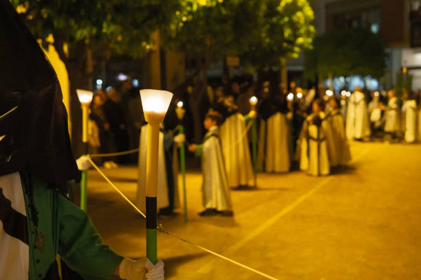 porträt eines unbekannten "capirucho"-anhängers, der den weg in einer prozession der stechpalmenwoche erhellt. grünes schwarz-weißes gewand und kapuze. kopieren von speicherplatz - church religion spirituality holly stock-fotos und bilder