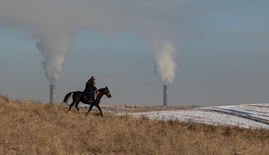 Almaty, Kazakhstan. 21.01.2021.
A rider on a horse rides across the steppe against the background of the smoking chimneys of a coal power plan