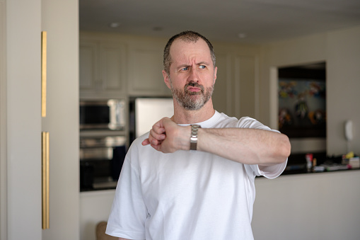 Annoyed man at home with white t-shirt looking up from his watch.