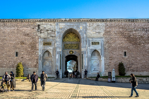 Istanbul, Turkey - February 9, 2024: Tourists walking in and out the Imperial Gate, the main entrance in the the first courtyard of Topkapi Palace.