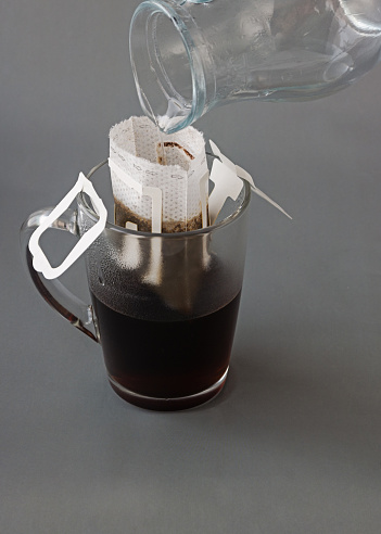 Making espresso coffee using a filter bag. Glass of black coffee on a gray background.
