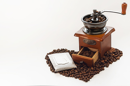 Filter bag with ground coffee, manual coffee grinder on a white isolated background. Copy space. Coffee beans laid out on the surface in the shape of a heart.