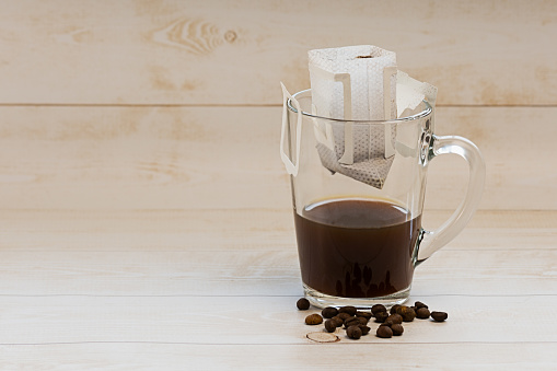 Preparing espresso coffee using a filter bag. Glass of black coffee on wooden background