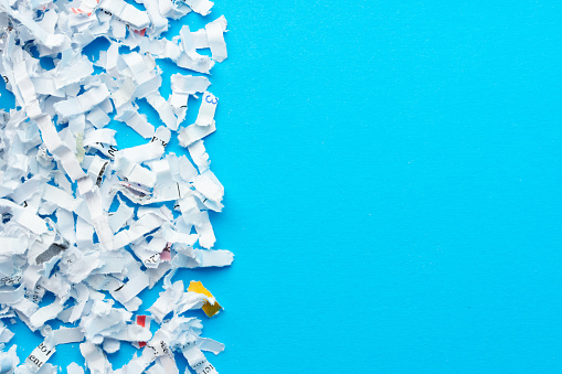 Close up image of a pile of shredded paper documents in front of a paper shredder.