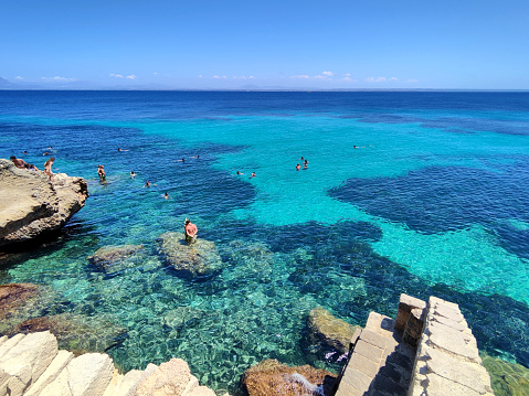 People bathing on the famous Cala del Bue Marino, a cliff with adjoining cave located on the island of Favignana in the Egadi Archipelago, Sicily, Italy.