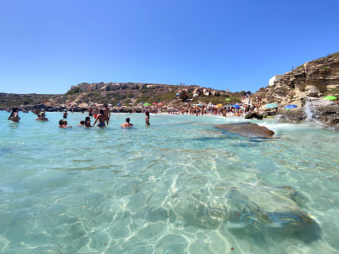 People bathing on the turquoise waters at the busy Cala Azzurra, a famous beach on the island of Favignana in the Egadi Archipelago, Sicily, Italy.