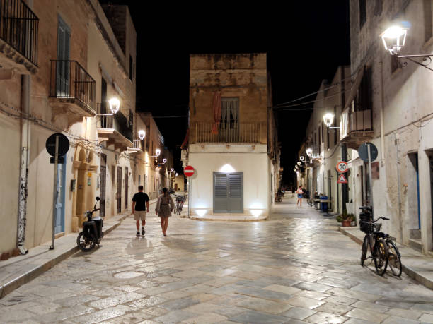 People walking on a street at night in Favignana, Egadi Archipelago, Sicily, Italy.