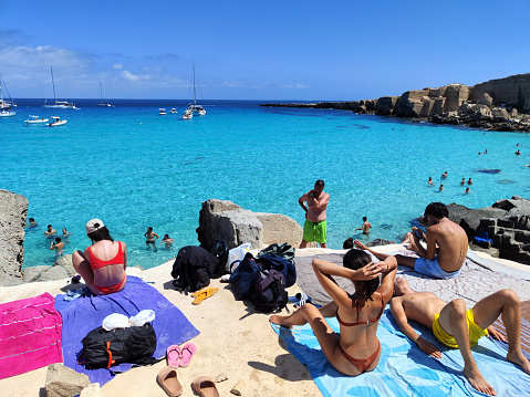 Crowd of tourists sunbathing at idyllic Cala Rossa, on the island of Favignana in the Egadi Archipelago, Sicily, Italy.