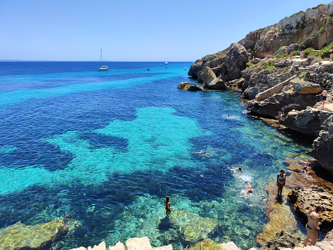 People bathing on the transparent turquoise waters at Cala del Bue Marino, a cliff with adjoining cave located on the island of Favignana in the Egadi Archipelago, Sicily, Italy.