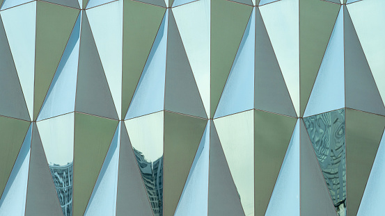Triangular building facade made of green glass, glass facade of modern building, Modern office building glass An architectural detail in green tones. Abstraction.