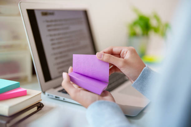 In the cropped image, a teenage Asian girl is seen using adhesive notes while studying for an exam. This demonstrates her proactive approach to studying, as she uses the notes to organize key information and aid in her preparation.