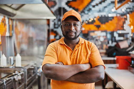 Portrait, fast food and confident black man at restaurant chain with small business owner at counter. Franchise, entrepreneur and store manager in kitchen service with arms crossed for hospitality.