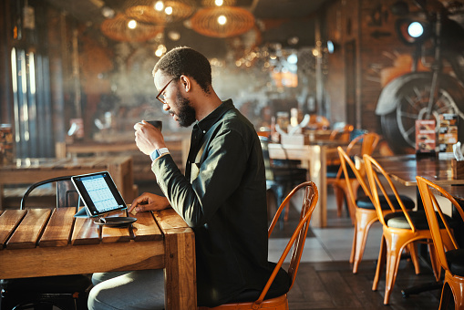 Black man, tablet and coffee at restaurant for small business, research or remote work on dining table. African male person or freelancer on technology with latte, cappuccino or cup of tea at cafe