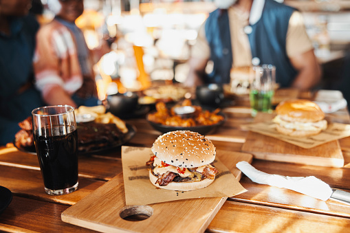 Burger, fast food with lunch or dinner on table at restaurant, people eating for nutrition and wellness with time together. Catering, hospitality and cuisine with barbecue sandwich meal at diner