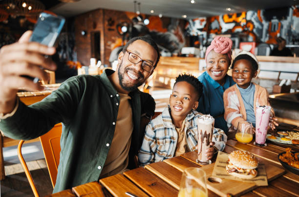 Family, selfie and eating at restaurant, happy for social media post and memory with parents and kids bonding. Smile for profile picture, photography and black people with food for nutrition at diner familia, selfie y comer en el restaurante, feliz por la publicación en las redes sociales y el recuerdo con padres e hijos uniéndose. sonrisa para foto de perfil, fotografía y personas negras con comida para la nutrición en el restaurante