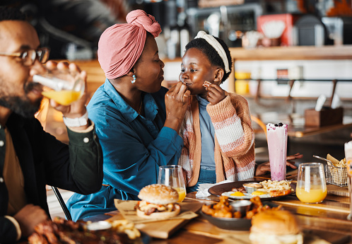 Black family, restaurant and eating with mom and child together with bonding, food and care. Love, diner and table with burgers and happy girl with lunch and hungry people in a cafe with drink
