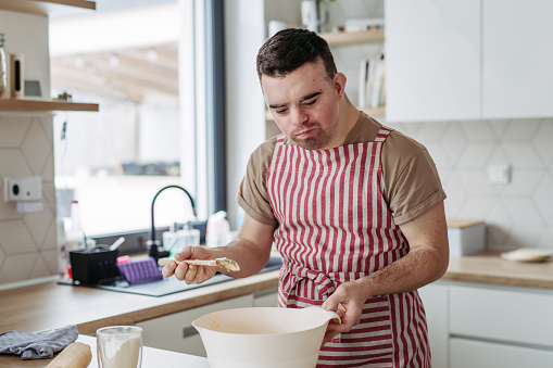 Young man with Down syndrome baking cookies at home. Everyday routine for man with Down syndrome genetic disorder.