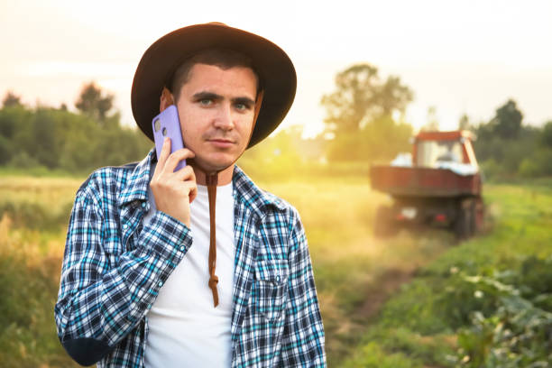 istock Young farmer talking phone on tractor background. Amidst a vast field, a farmer confidently walks, multitasking as he engages in a conversation on a purple phone against the backdrop of a tractor 2032140620