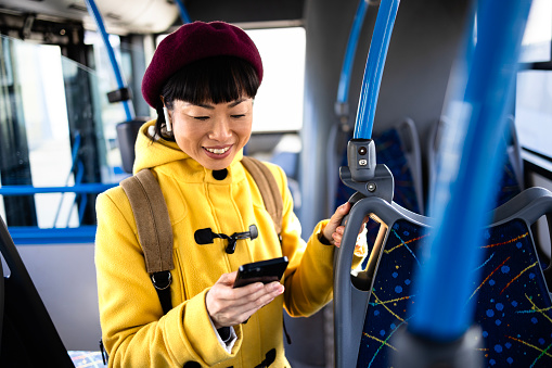 Smiling woman using smart phone while traveling by public bus.