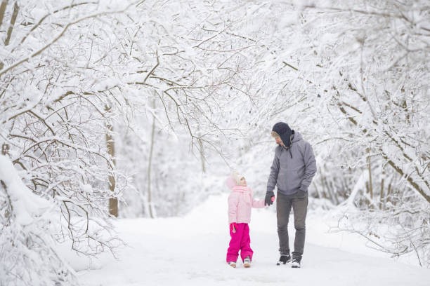 Smiling father and daughter walking on white fresh snow covered road through tree branches at park after blizzard. Spending time together in beautiful winter day. Enjoying nature stroll. Front view.