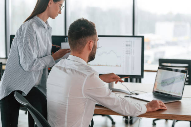 istock Brokers with monitors with graphs on the table. Two employees are working in the office together 2032159289