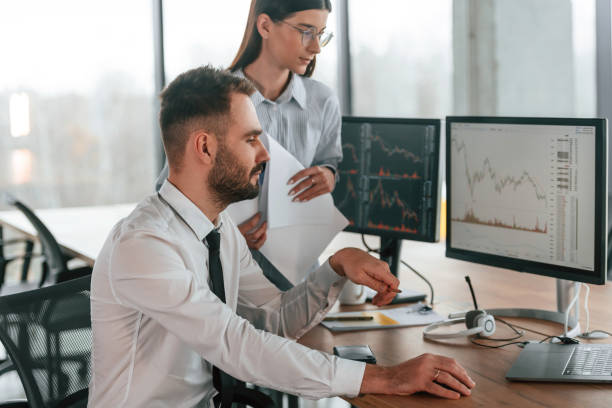 istock Brokers with monitors with graphs on the table. Two employees are working in the office together 2032159290