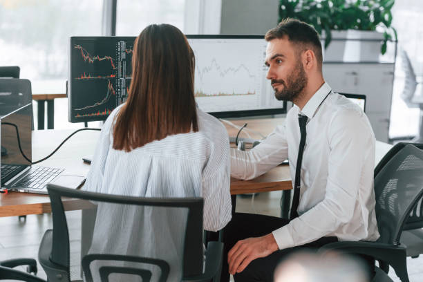 istock Brokers with monitors with graphs on the table. Two employees are working in the office together 2032159296