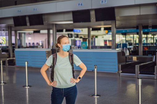 Woman in mask at empty airport at check in in coronavirus quarantine isolation, returning home, flight cancellation, pandemic infection worldwide spread, travel restrictions and border shutdown.