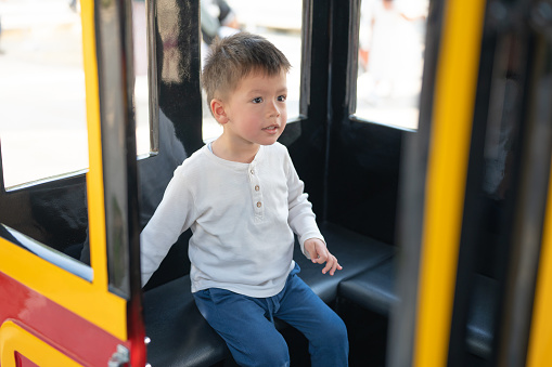 A happy toddler enjoys a delightful train ride through the park, captivated by the colorful surroundings and gentle motion. A two and half year old multiracial young boy eagerly gazes out the train window,as he embark on a journey through the was park during a weekend fun activity