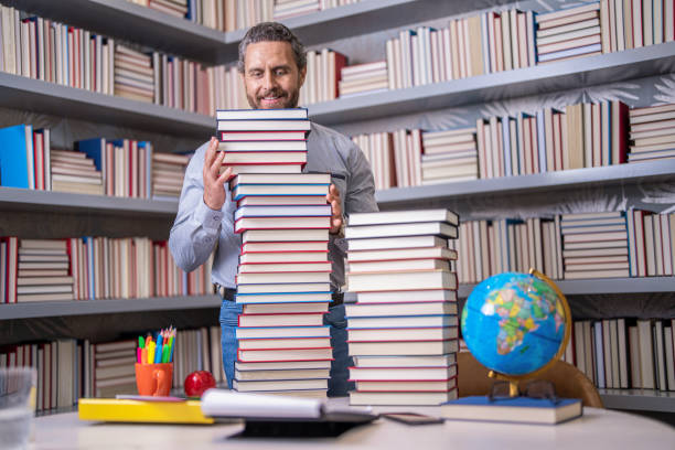 istock Man with books in library. Knowledge and education. Absorbed in a book. school library. Teachers day. Teacher in school classroom. teacher with book in library classroom. Hispanic teacher in college 2032177420