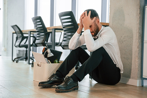 Depressed, sitting on the floor. Unemployed man is with personal belongings after being fired.