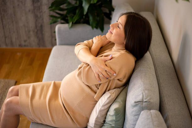 istock Pregnant woman hugging self while sitting on sofa 2032197088