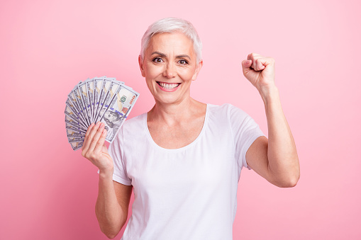 Photo portrait of pretty retired female hold money fan raise fist winner wear trendy white outfit isolated on pink color background.