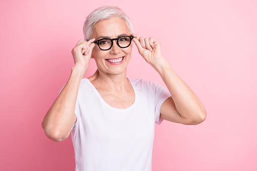 Photo portrait of pretty retired female touch specs check vision toothy smile wear trendy white outfit isolated on pink color background.