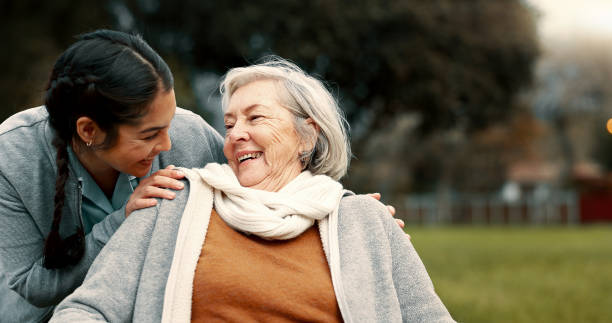 caregiver helping woman with disability in park for support, trust and care in retirement. nurse talking to happy senior patient in wheelchair for rehabilitation, therapy and conversation in garden - ouderenzorg stockfoto's en -beelden