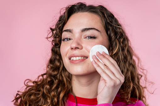 Curly-haired woman gently applying a cotton pad to her face, skincare routine