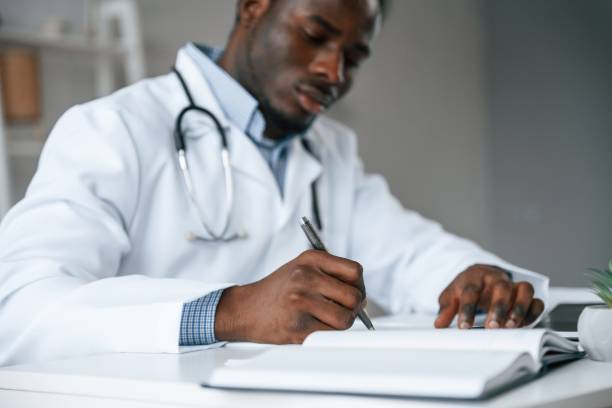 istock Filling in the document, writing by using pen. Black man as doctor in the clinic office 2032248932
