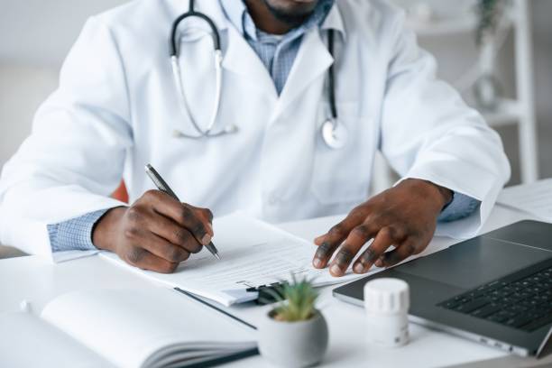 istock Filling in the document, writing by using pen. Black man as doctor in the clinic office 2032248937