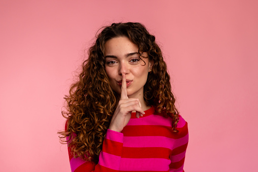 Curly-haired woman with finger on lips signaling to keep a secret.