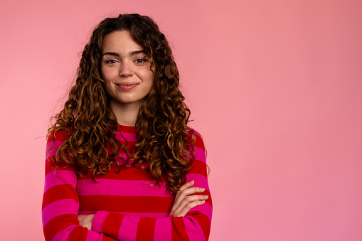 Content young woman smiling with arms crossed on a pink background.